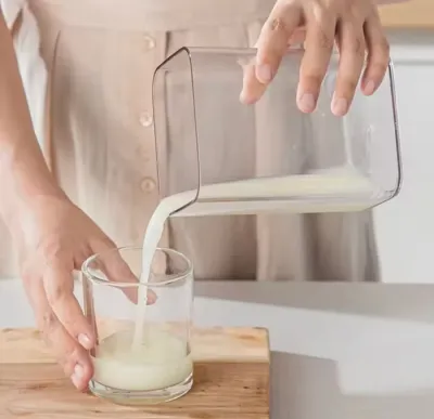 Pouring filtered whey liquid from the outer transparent container of the Greek Yogurt Strainer into a clear glass.