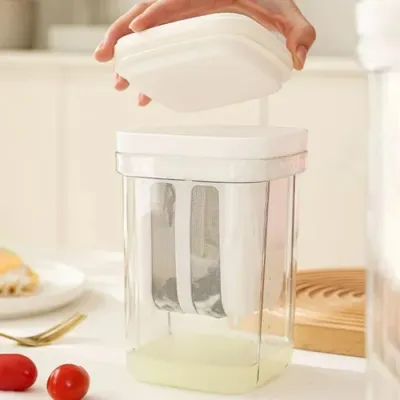 A hand placing the white lid onto the clear Greek Yogurt Strainer filled with straining liquid on a kitchen table.