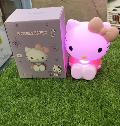 Pink glowing Hello Kitty Silicone Night Lamp placed on green grass next to box.