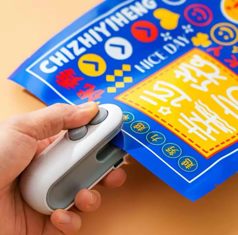 A hand using a white and grey Mini Bag Sealer 2 in 1 Heat Sealer and Cutter on a colorful plastic snack pouch.
